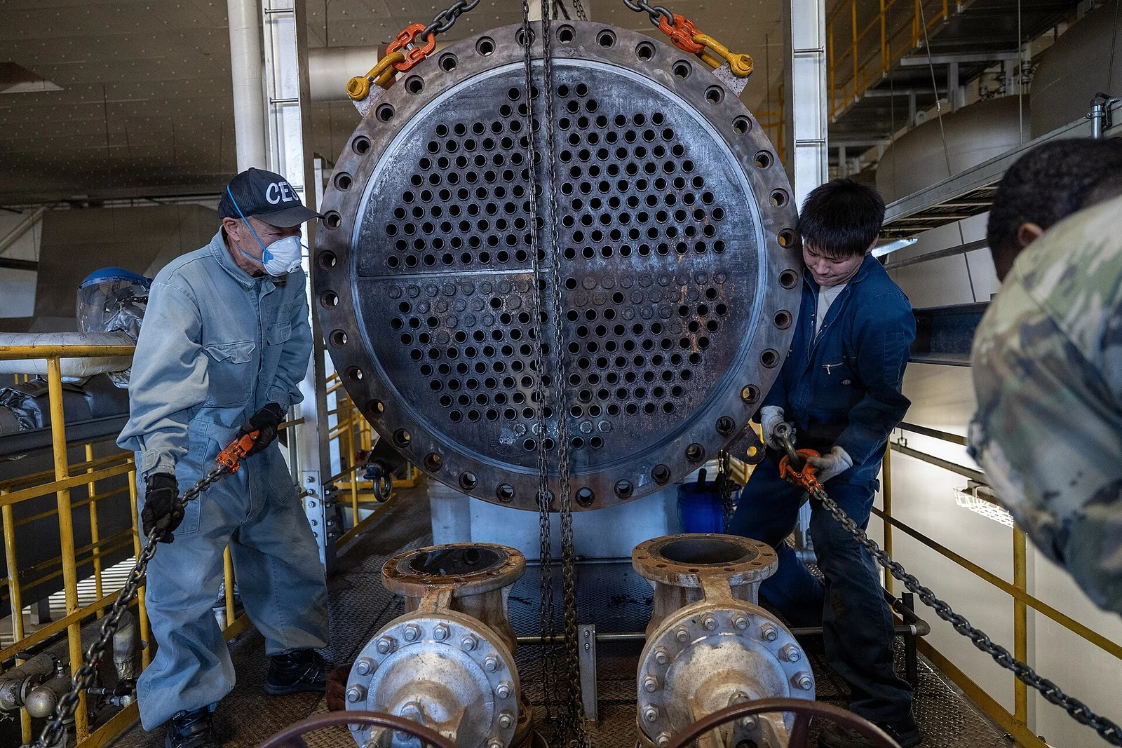 Techniciens manipulant un élément d’une chaudière lors d’une réparation.